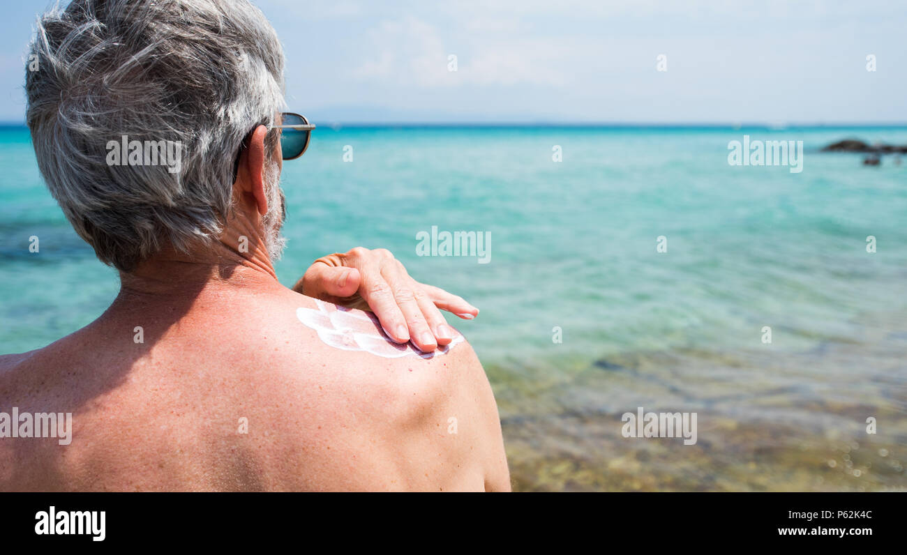 Hombre Senior aplicar loción de sol en vacaciones de verano vista posterior Foto de stock
