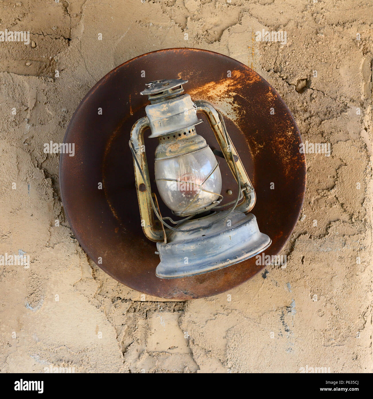 Linterna de antigüedades con reflector oxidado colgado en una pared de adobe Foto de stock