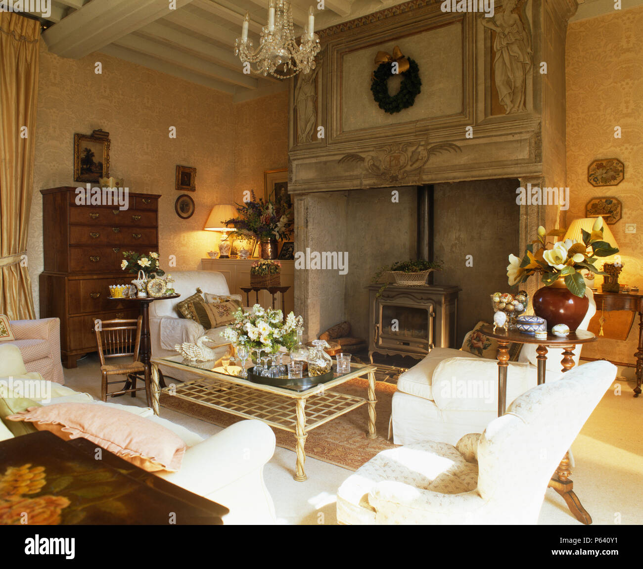 Chimenea de madera tallados ornamentados con estufa de leña en el país francés salón con sofás blancos y muebles antiguos Foto de stock