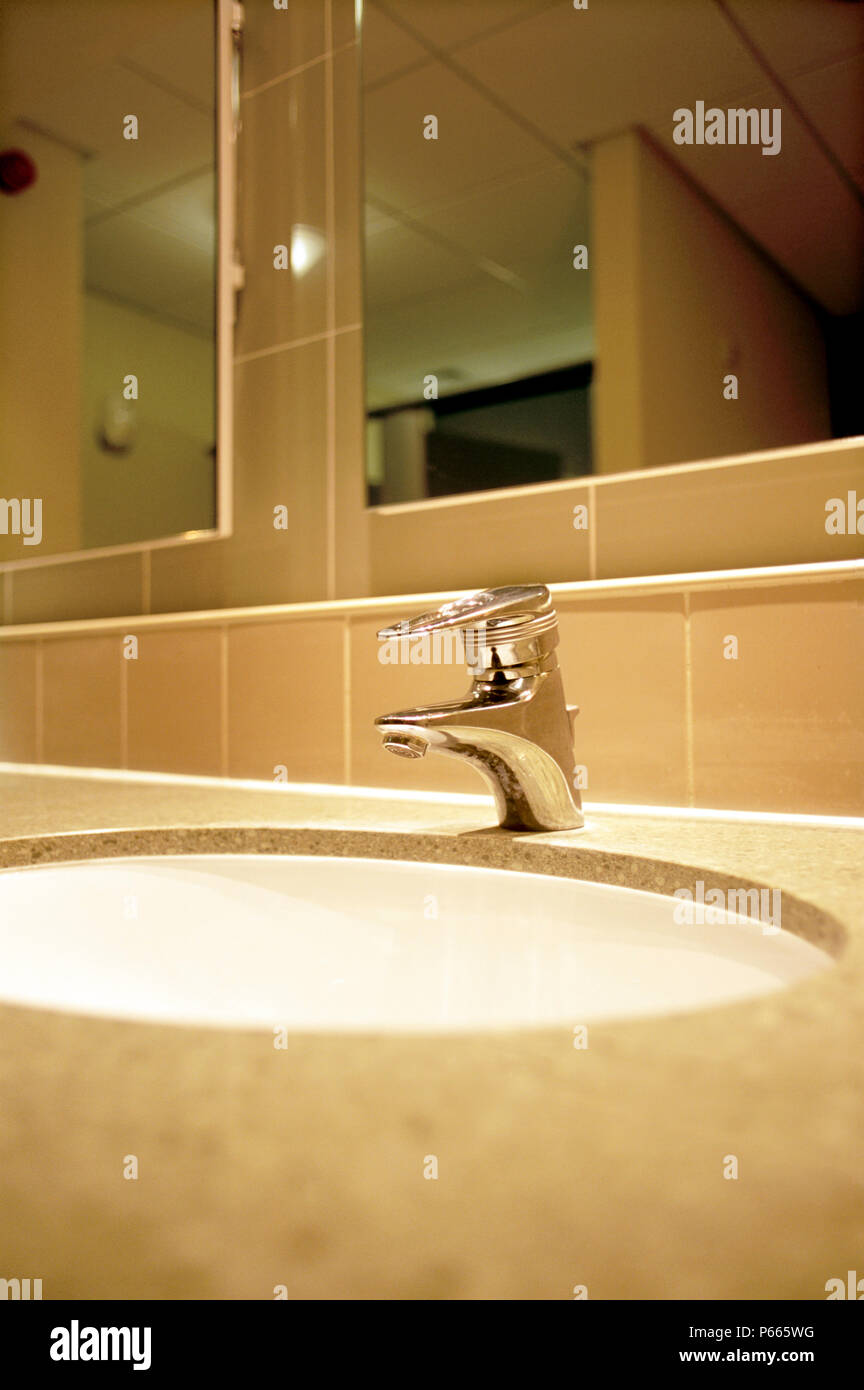 Detalles dentro de aseos, mostrando taps, lavabo, espejo y superficies de mármol. Foto de stock