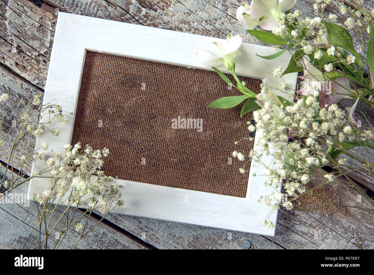 Marco de fotos en blanco y flores blancas sobre fondo de tabla de madera Foto de stock