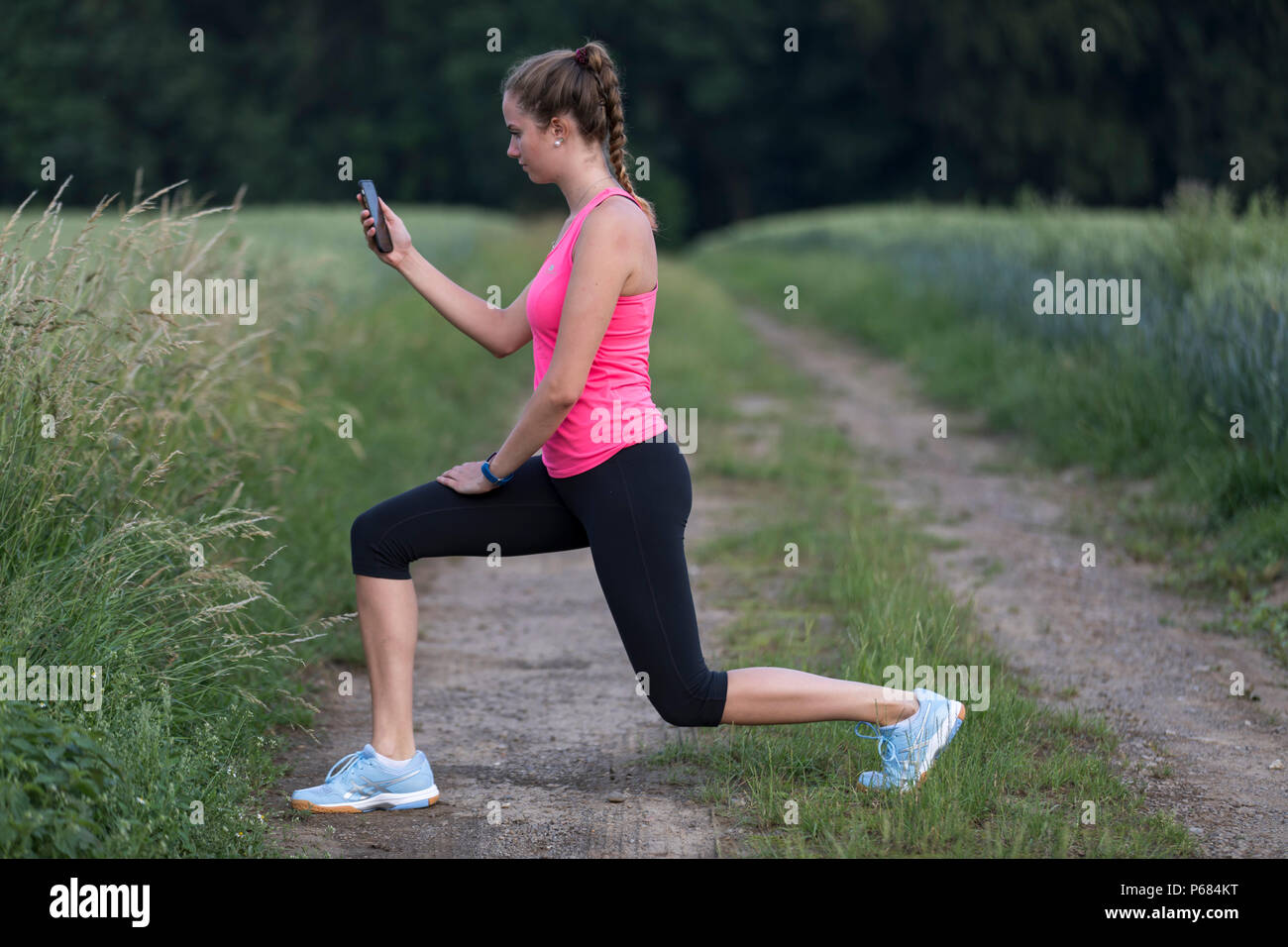 Mujer joven hacer ejercicios de estiramiento, correr, trotar, viendo los ejercicios en una aplicación, en un teléfono móvil, smartphone Foto de stock