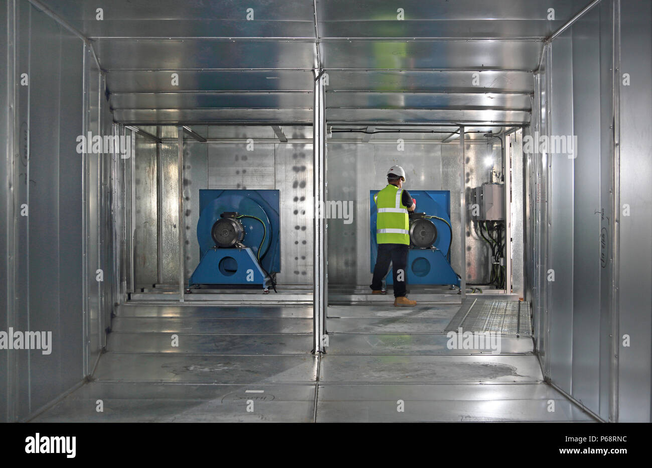 Un ingeniero trabaja en el motor del ventilador gigante dentro de un conducto de aire acondicionado durante la construcción de un nuevo edificio de oficinas en Londres, Reino Unido Foto de stock
