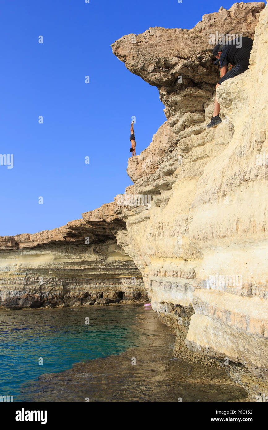 Un buzo masculino preparación para zambullirse desde los acantilados en el agua color turquesa en el mar las cuevas cerca de Cape Greco, Chipre Foto de stock