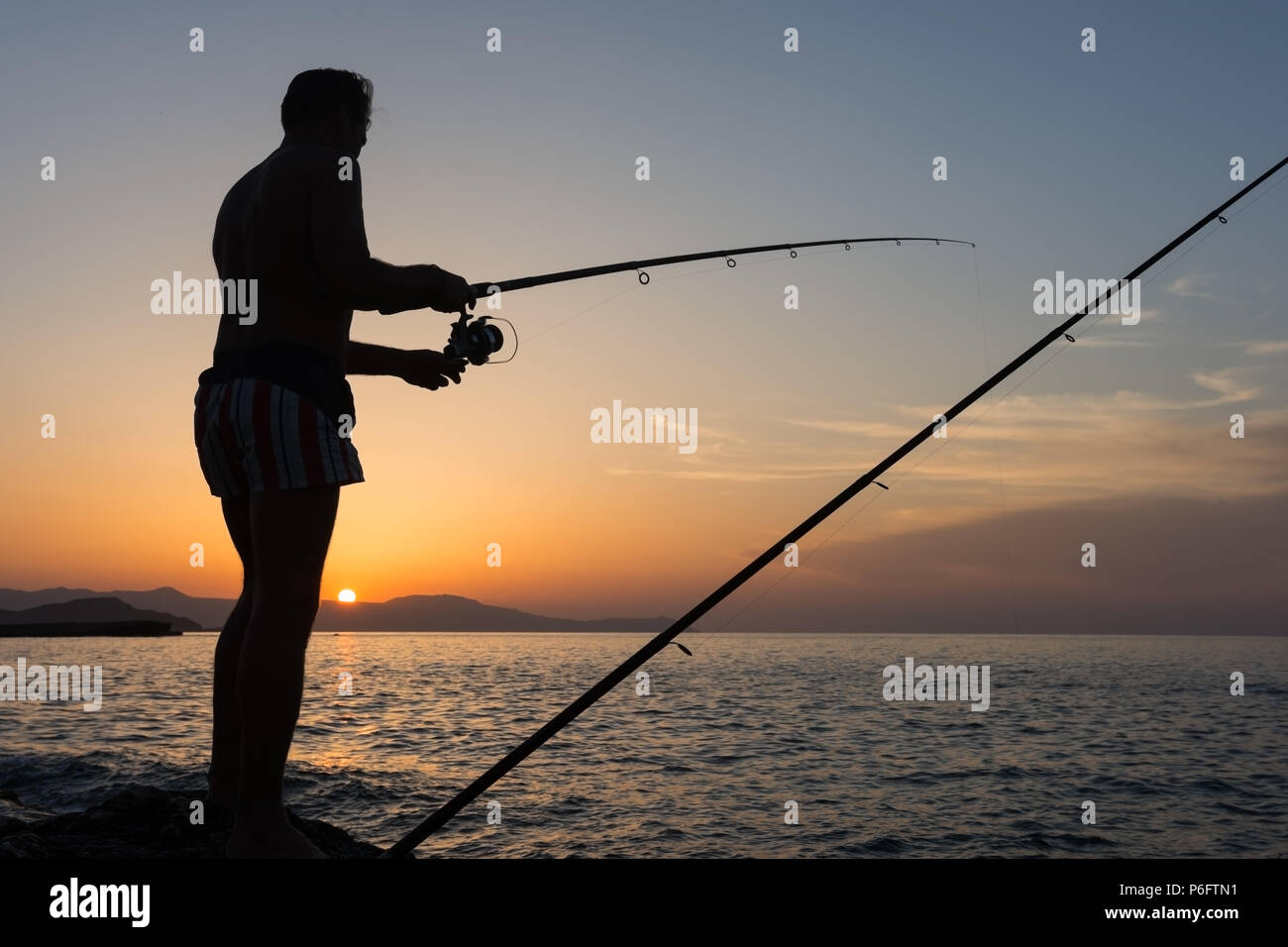 Hombre con varilla de pesca en el mar al atardecer, verano en Grecia Foto de stock