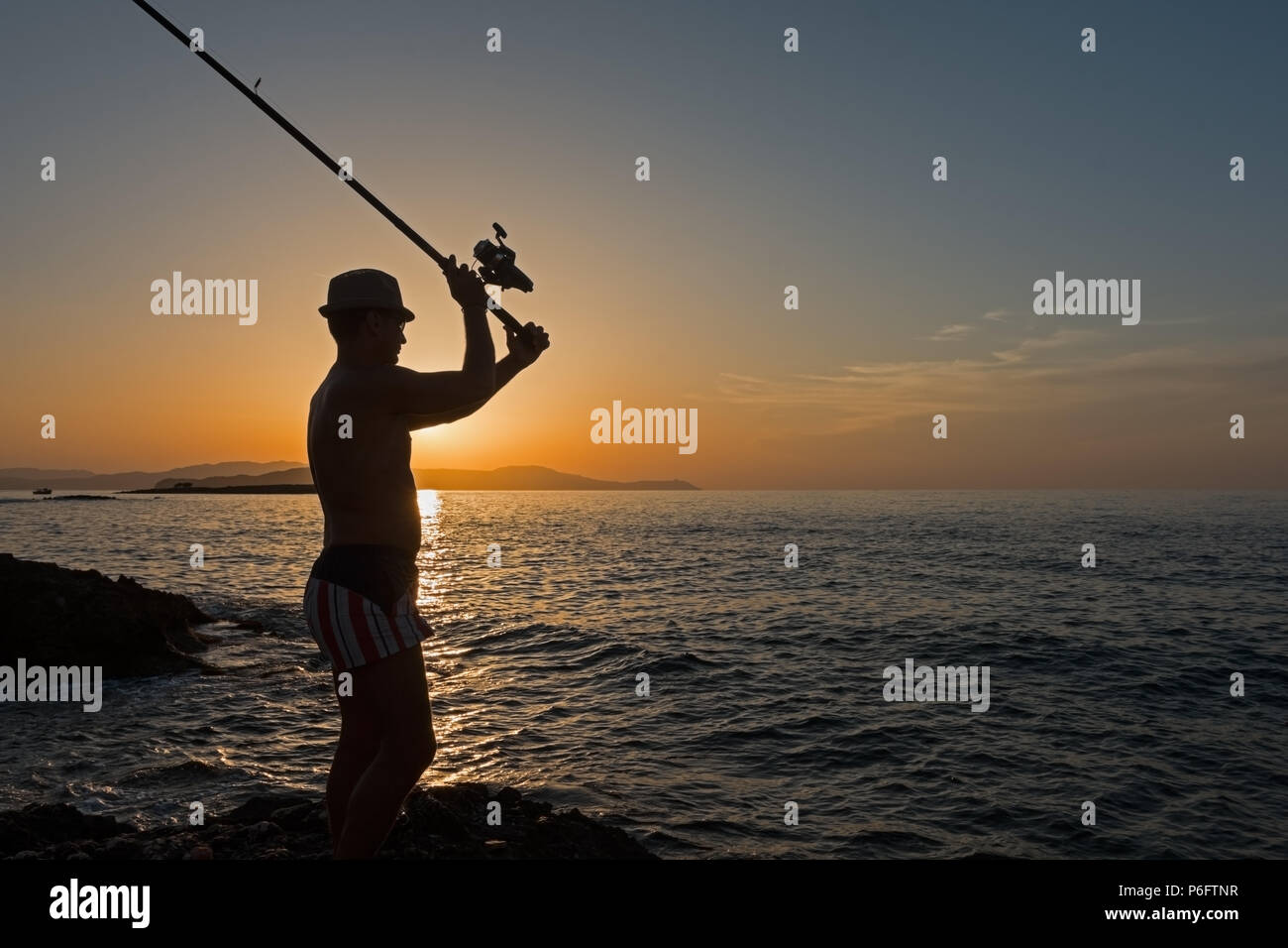 Macho adulto lanza la caña de pescar en el mar Foto de stock