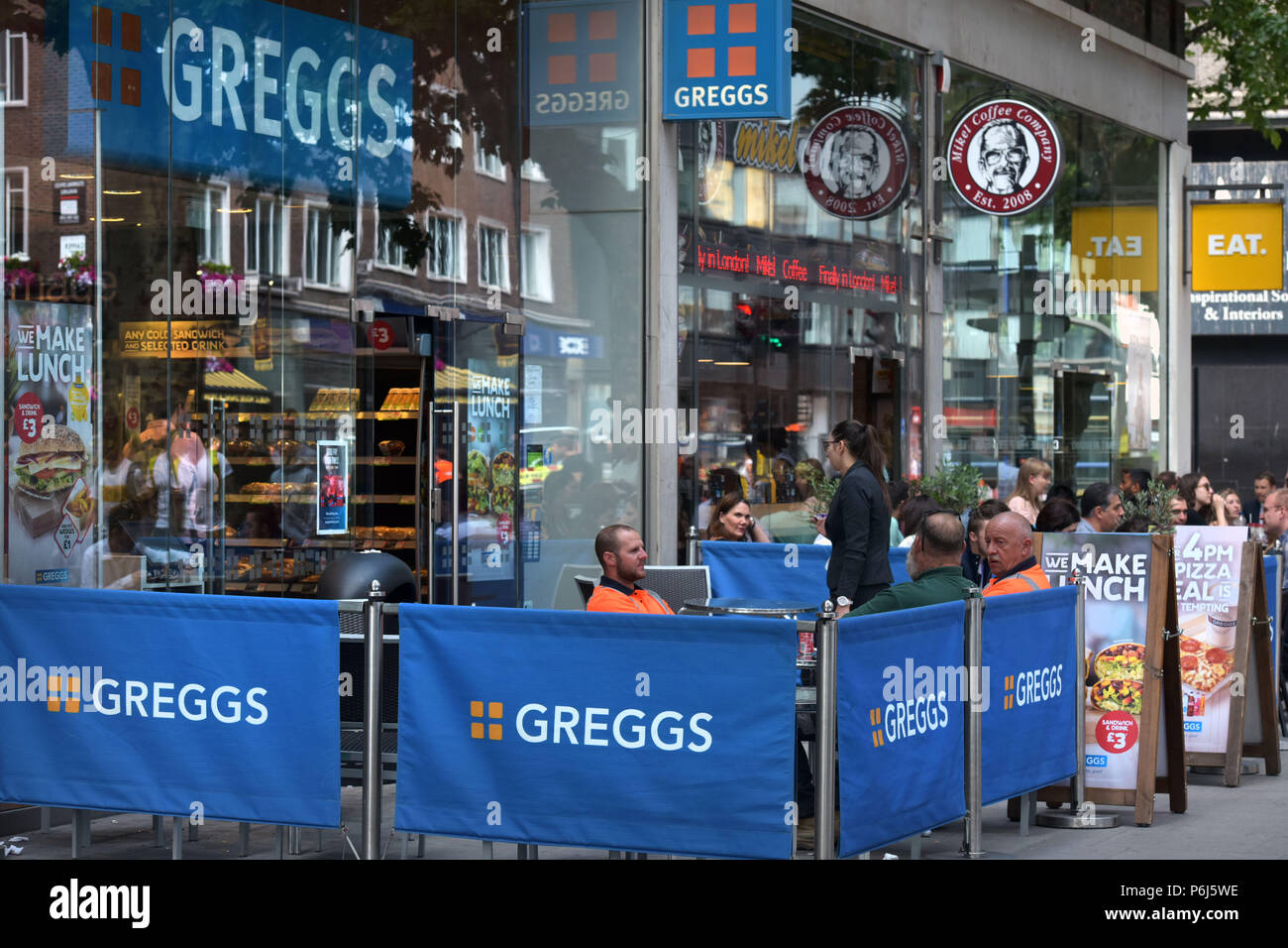 Las personas sentarse fuera una hilera de cafés y tiendas de comida
