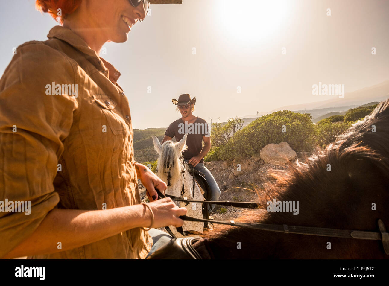 Bonito par vaqueros caucásica cabalgar en el viento ladscape pintoresco lugar. Mujer y hombre juntos divertirse con terapia de caballos y disfrutar del atardecer de SMIL. Foto de stock