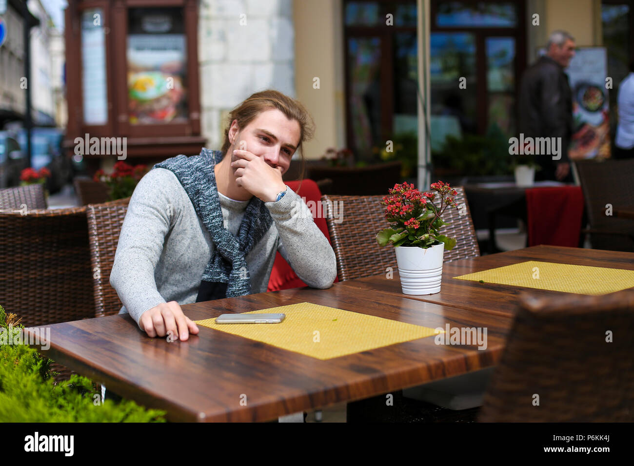 Empresario joven sentado en la cafetería de la calle y vestidos de suéter gris. Foto de stock