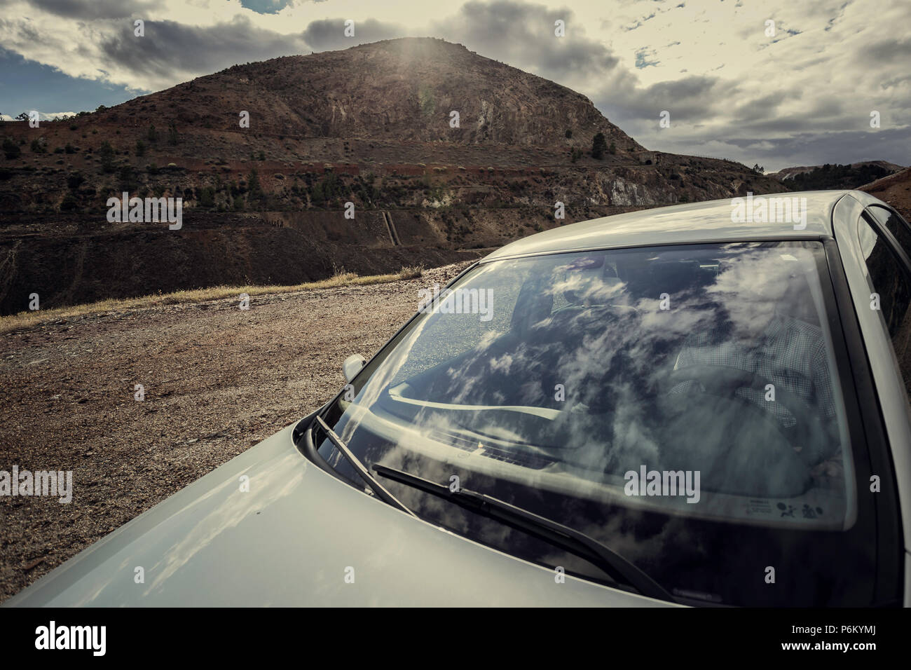 Las nubes se refleja en el cristal delantero del vehículo gris con un hombre interior y montaña y cielo con nubes antecedentes en la zaranda minas, España Foto de stock