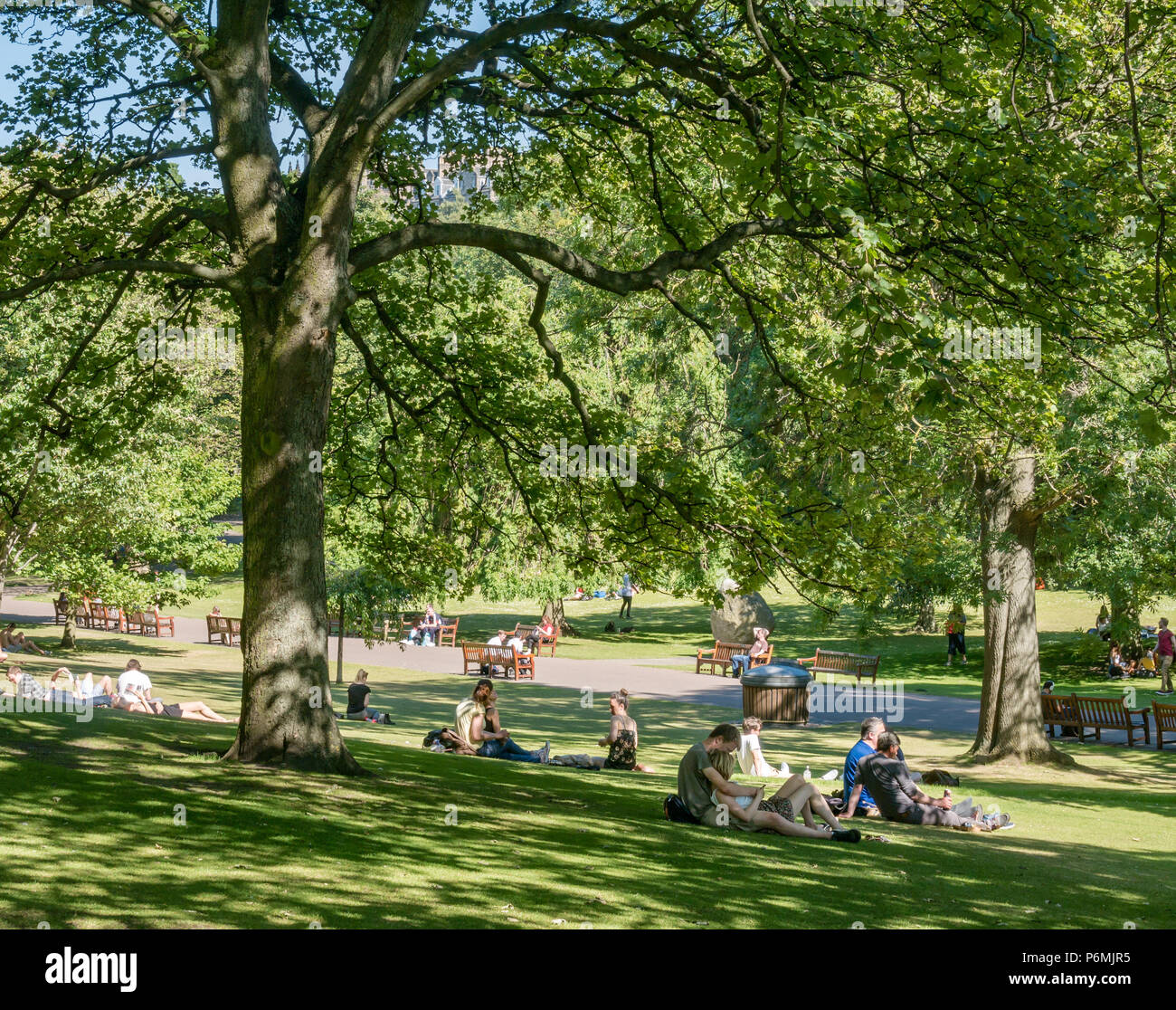 Par abrazando a sentarse en la hierba y la gente descansando en los jardines de Princes Street en la sombra bajo los árboles durante la canícula, Edimburgo, Escocia, Reino Unido Foto de stock
