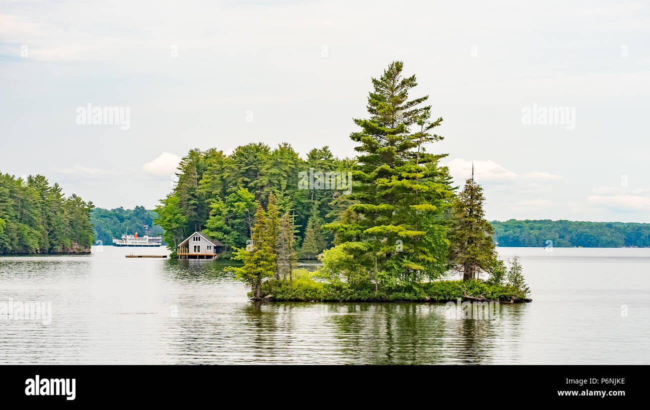 La pequeña isla en el lago Muskoka con una casita y excursión en barco en el fondo. Foto de stock