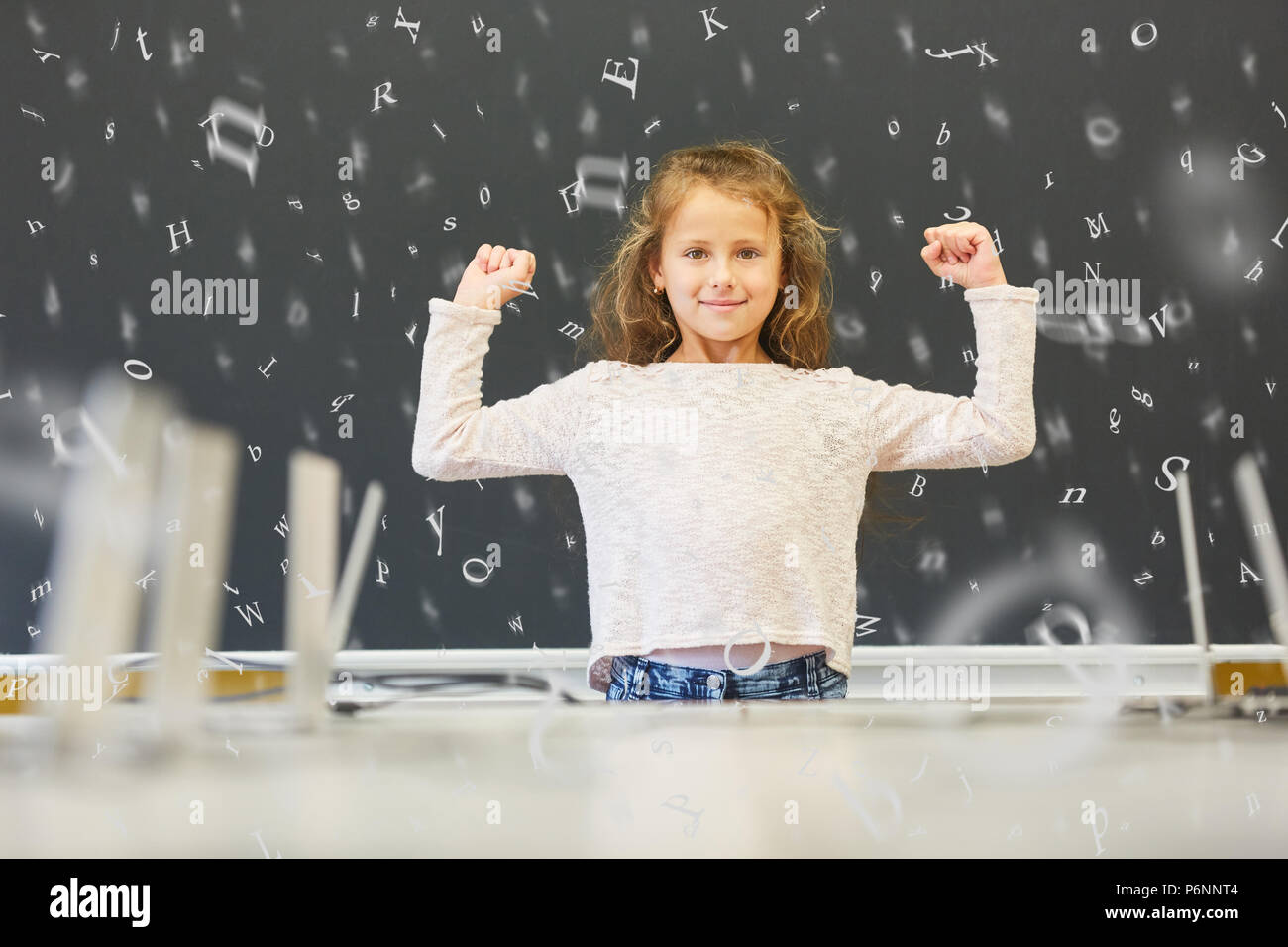 Chica fuerte está en la escuela primaria en frente de un pizarrón con muchas letras voladoras Foto de stock