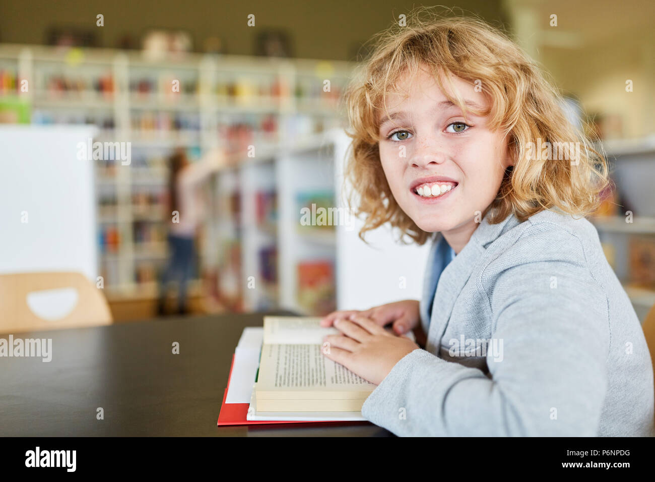 Feliz muchacho rubio está leyendo un libro en la biblioteca de la escuela primaria Foto de stock