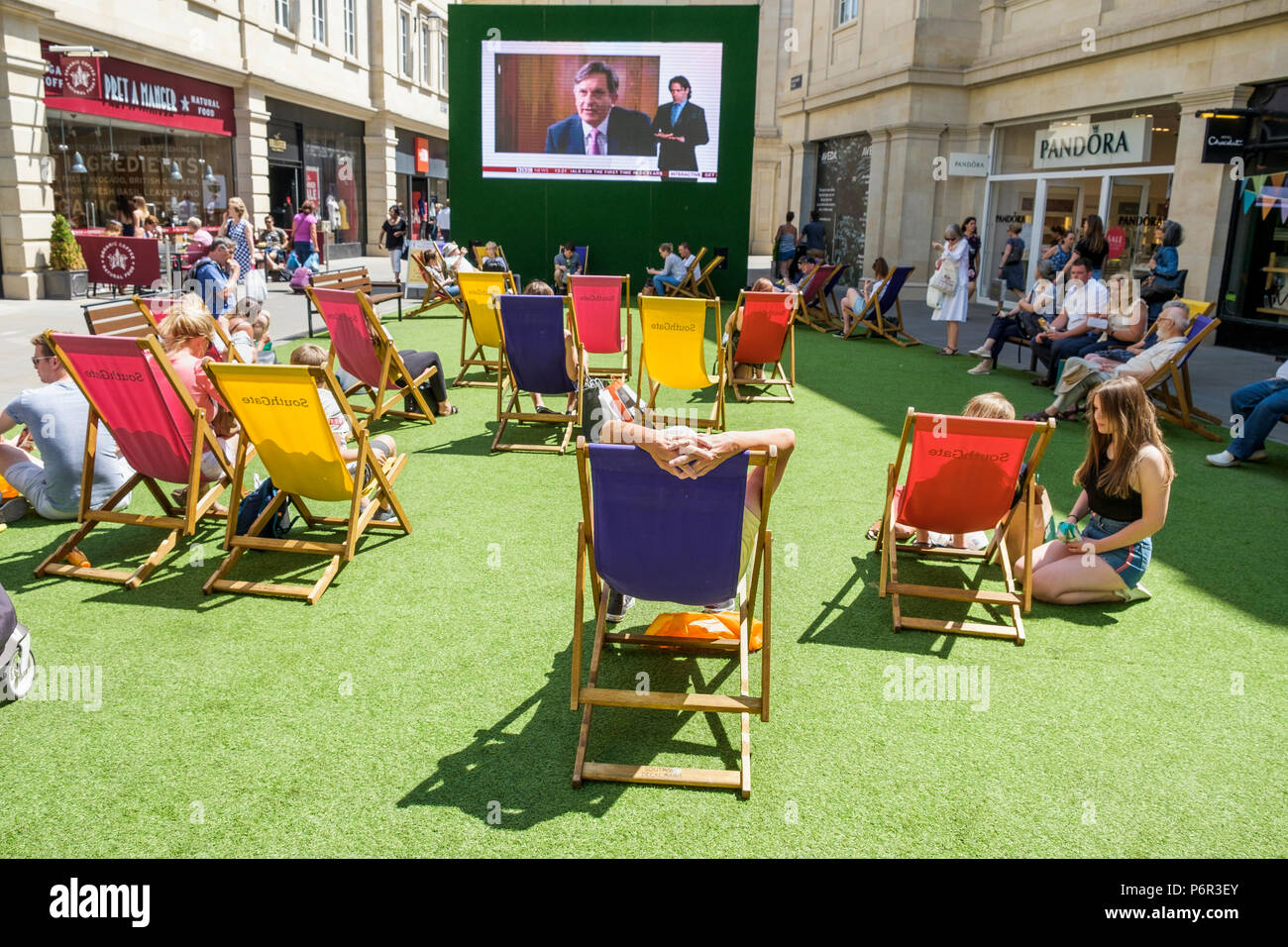 Bath, Reino Unido, 2 de julio, 2018. Como Bañera disfruta de otra muy caluroso y soleado día compradores son foto disfrutando del sol en SouthGate centro comercial donde una pantalla grande ha sido configurado para que los aficionados al tenis pueden ver el campeonato de tenis de Wimbledon, los meteorólogos predicen que el clima cálido continuará en la próxima semana. Foto de stock