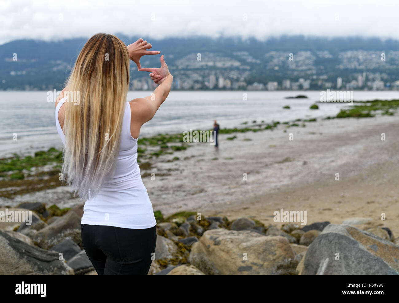 Mujer joven en la playa del Parque Stanley en busca de Vancouver, en la ladera de la colina y enmarcar la vista con las manos, tratando de imaginar un lugar agradable para vivir. Foto de stock