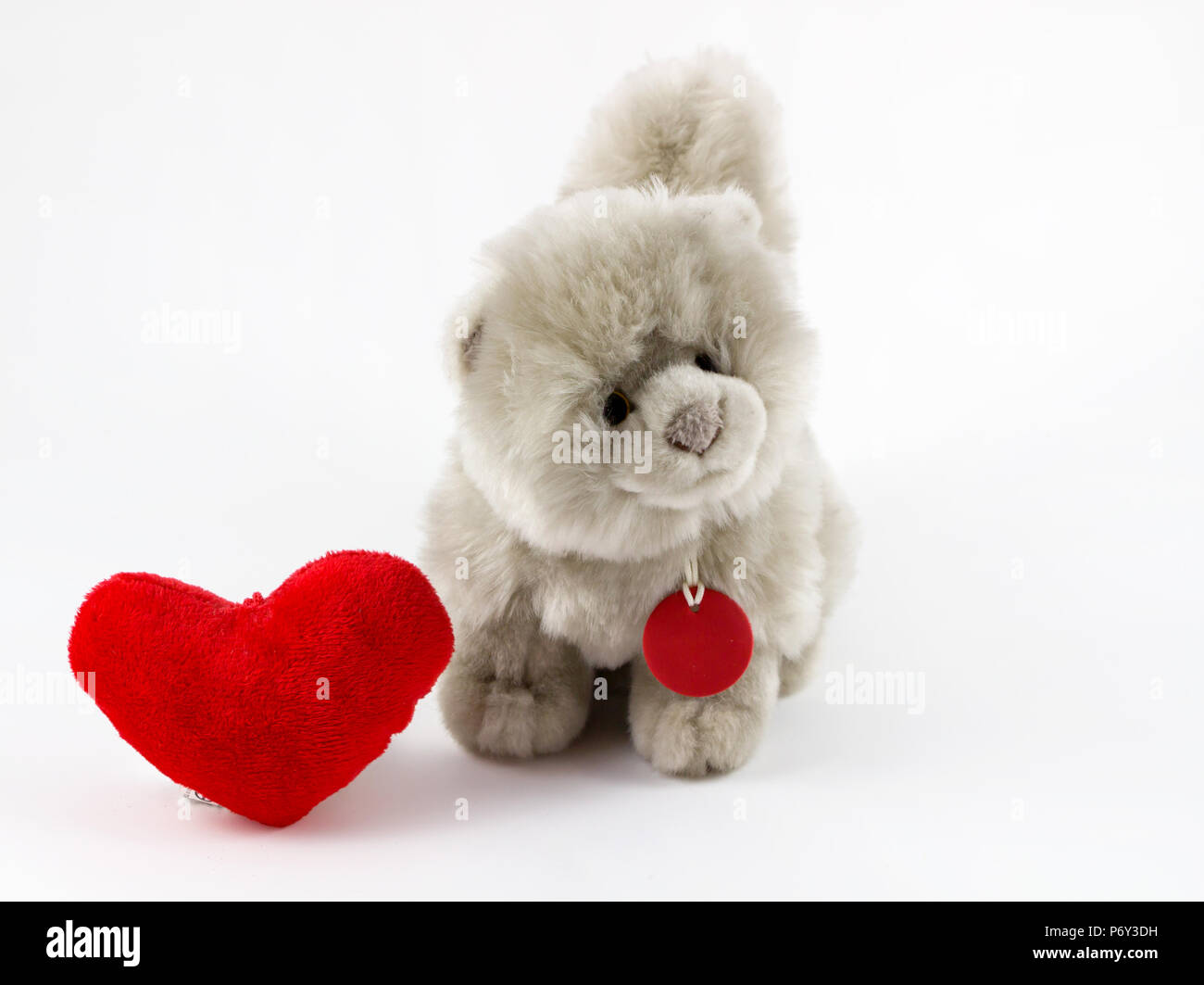 Peluche suave con corazón rojo sobre fondo blanco / Peluche Perro y corazón sobre fondo blanco / animal de juguete. Foto de stock