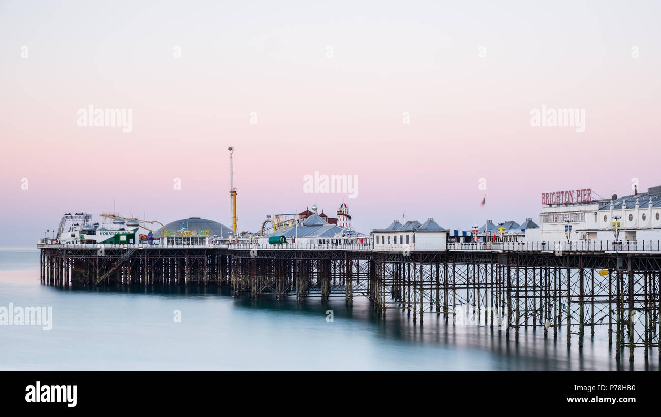 Brighton Pier (Muelle central) en Brighton, East Sussex, al amanecer, con coloridos tonos pastel en un cielo despejado y suave, agua azul tranquila Foto de stock