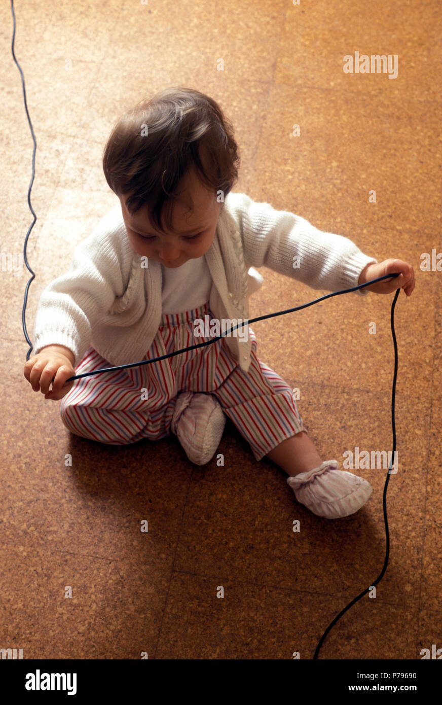Bebé sentado en el suelo jugando con el cable eléctrico en peligro de electrocución Foto de stock