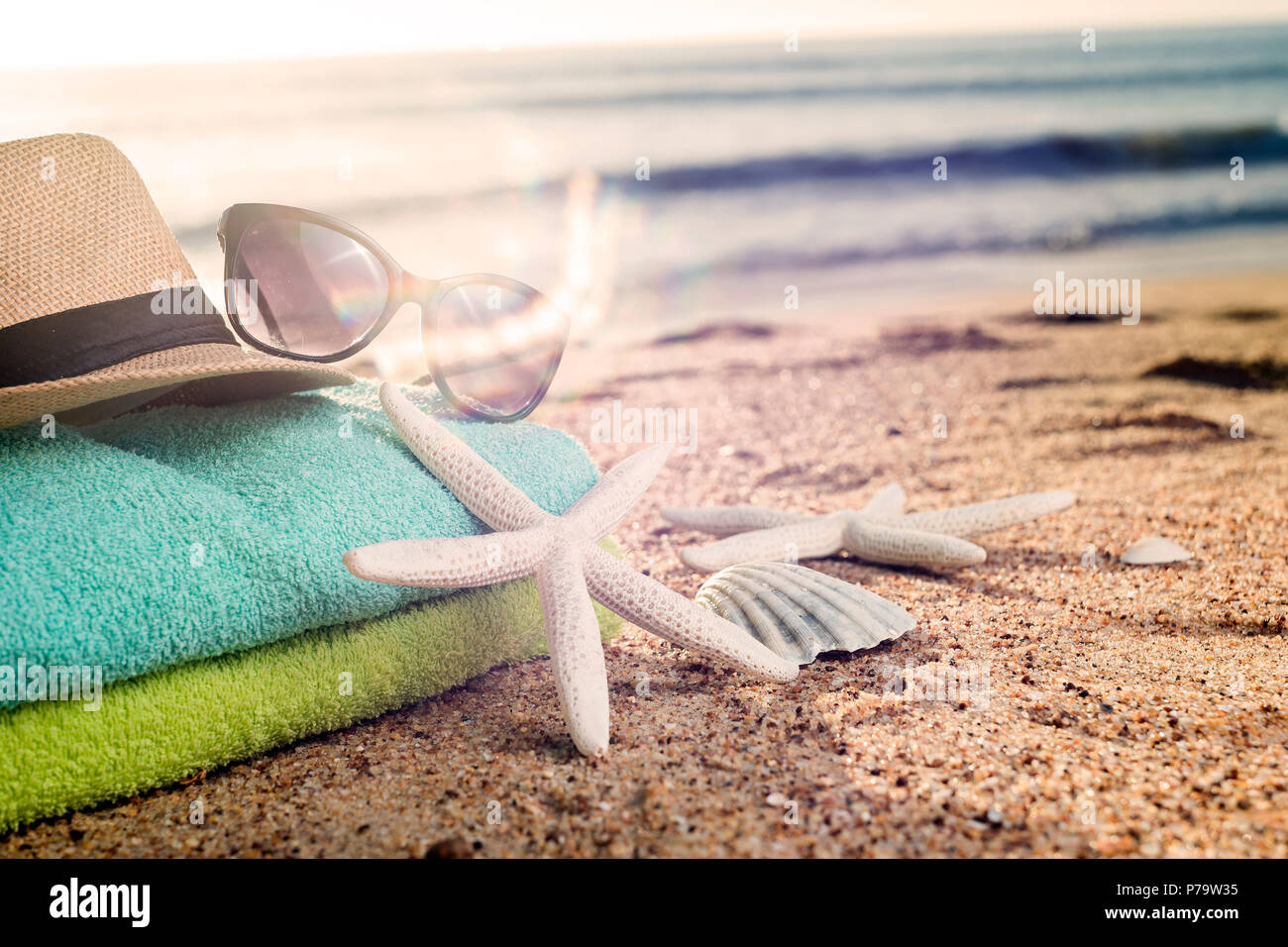 Accesorios de verano como coloridas toallas, sombrero de paja, gafas de sol y conchas en la playa Foto de stock