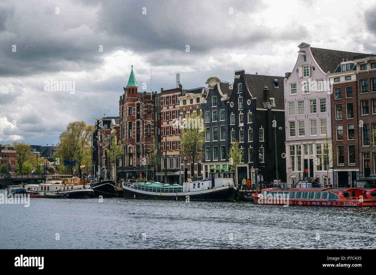 Amsterdam, Holanda - 27 de abril, 2017: Casas flotantes y viviendo barcazas en Binnenamstel canal contra casas de típica holandesa con pabellón de Países Bajos y Foto de stock