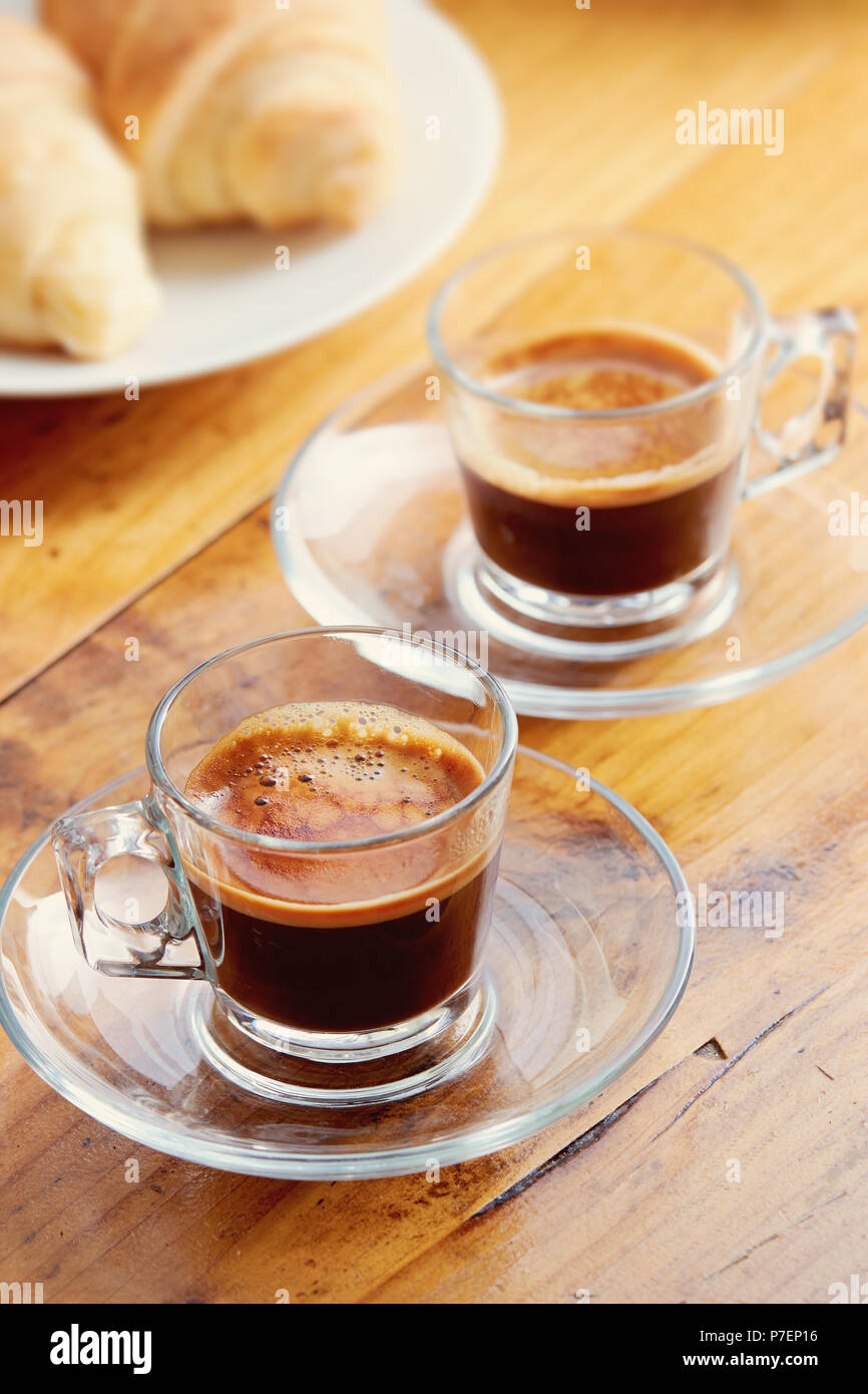 Dos tazas de café con un croissant en la mesa de madera antigua Foto de stock