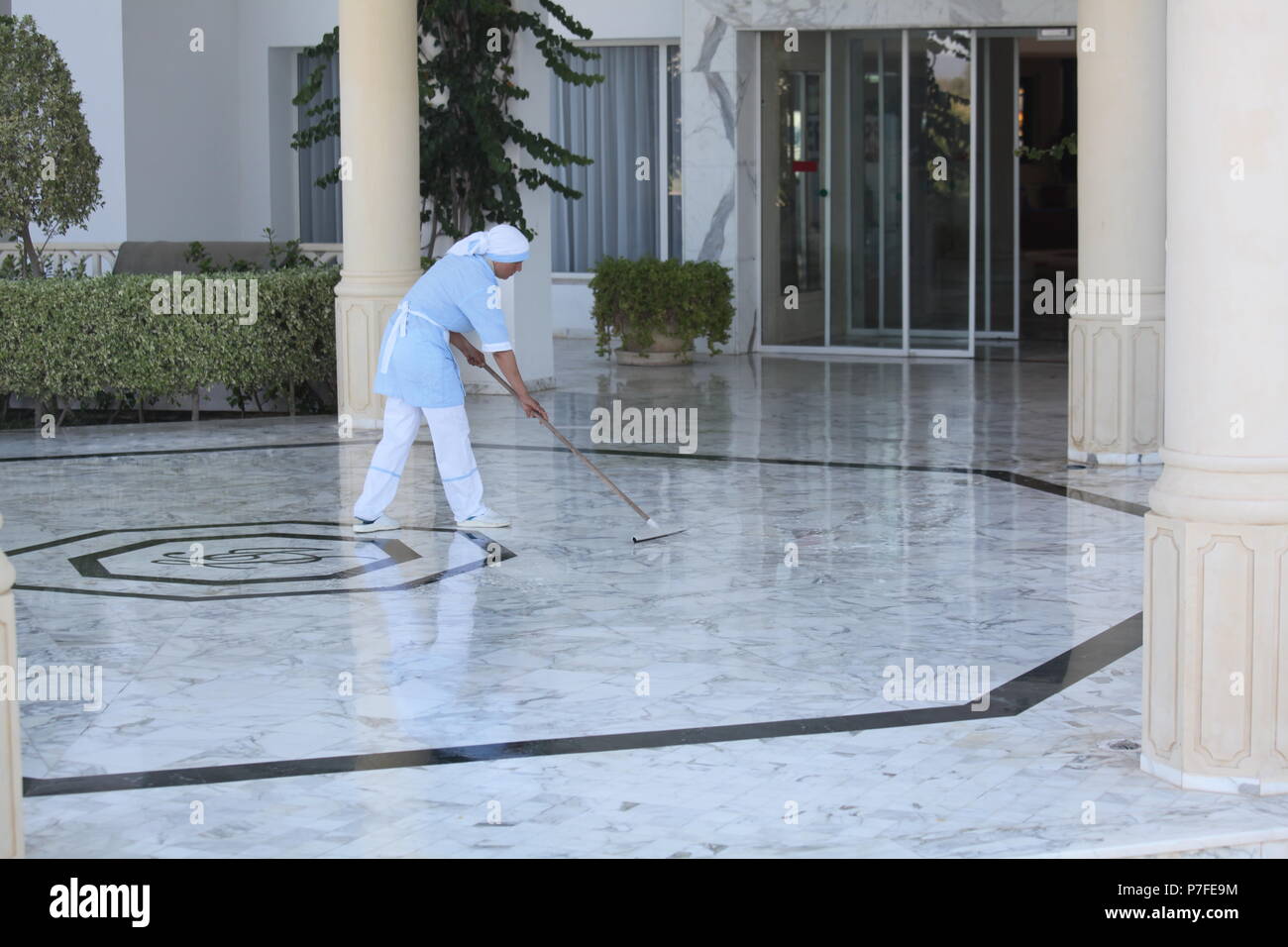 Vestidas con uniformes limpios local es la señora de la limpieza La limpieza piso de mármol en la entrada del hotel de 4* en Hammamet, gran centro turístico en Túnez Foto de stock