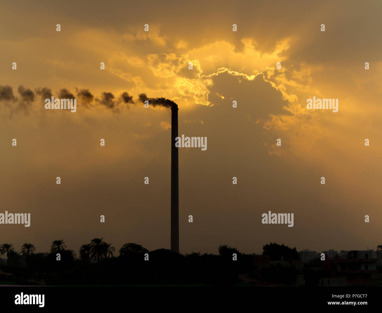 Atardecer sobre el río Nilo Egipto en una zona industrial con contaminación de fumar chimenea aumentando los espectaculares colores naranja en las nubes Foto de stock