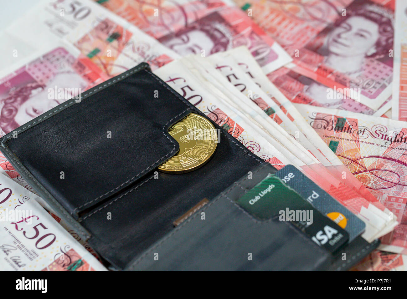 Un monedero conteniendo un bitcoin y 50 libras esterlinas billetes de banco en una gran pila de más cincuenta libras billetes usados Foto de stock