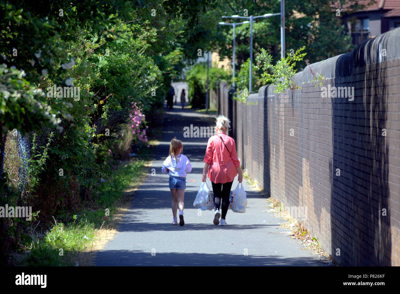 Madre e hija llevando bolsas de compras caminando por una calle estrecha soleado sombras de personas en primer plano el verano Foto de stock
