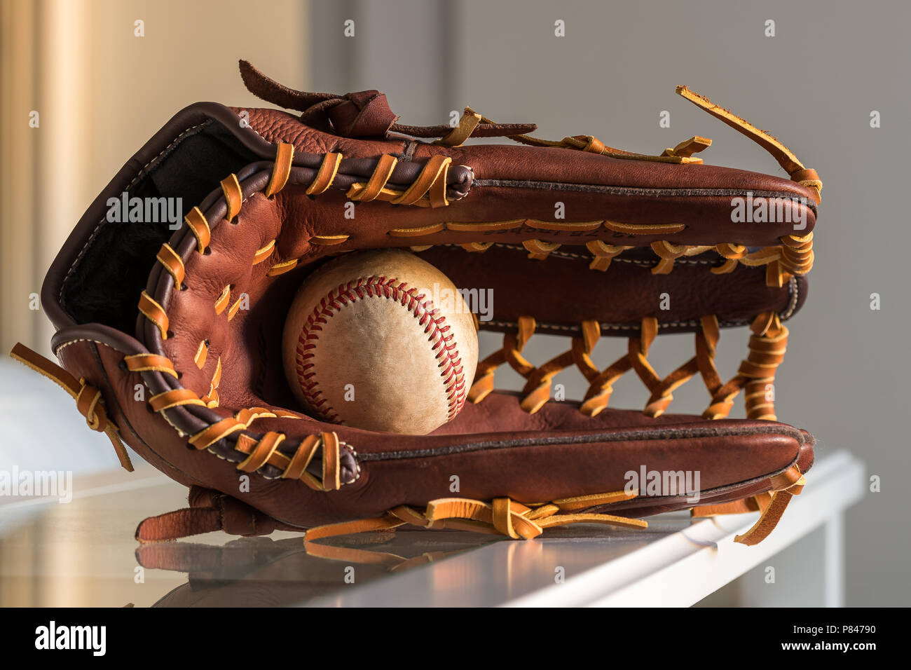 Close-up de una pelota de béisbol usado dentro de un guante de béisbol, cuero marrón sobre la llanura, fondo gris. Foto de stock