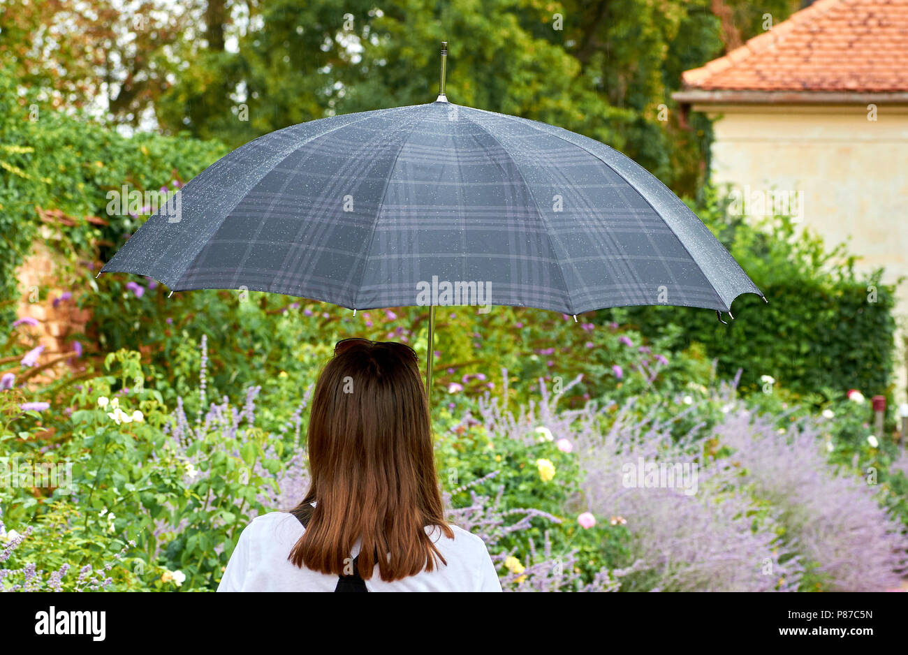 Mujer joven con sombrilla de pie en el jardín, rociar con gotas de agua sobre paraguas Foto de stock