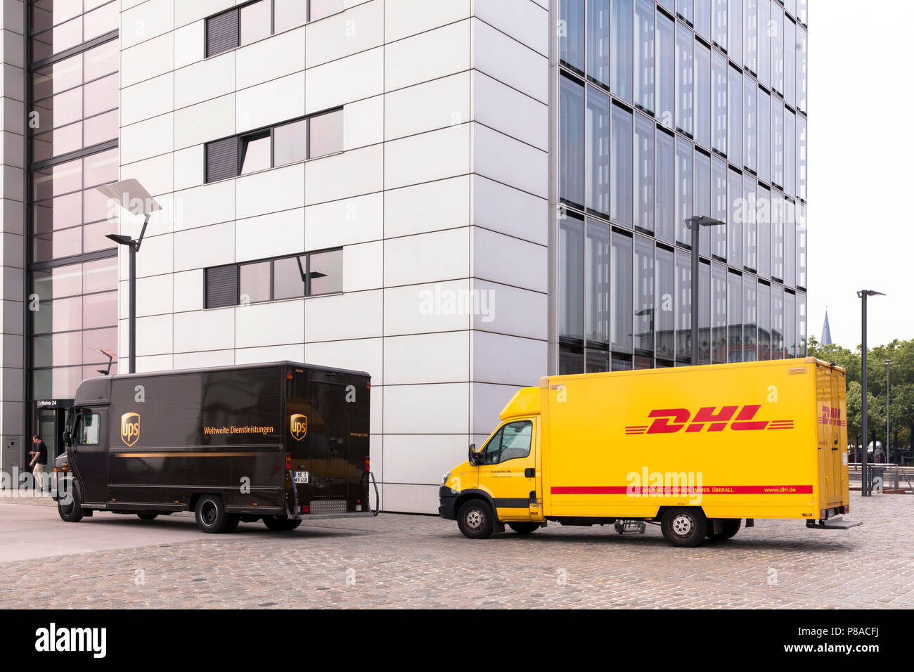 Servicio de paquetería DHL y UPS parcel service coches delante de la grúa en casa Sur Rheinau Harbour, en Colonia, Alemania. DHL und UPS Fahrzeuge vor dem Kranh Foto de stock