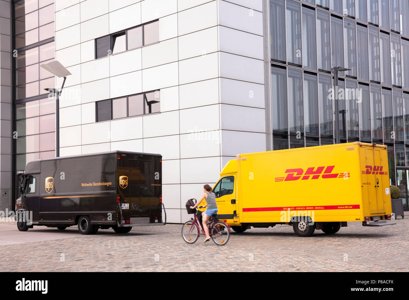 Servicio de paquetería DHL y UPS parcel service coches delante de la grúa en casa Sur Rheinau Harbour, en Colonia, Alemania. DHL und UPS Fahrzeuge vor dem Kranh Foto de stock
