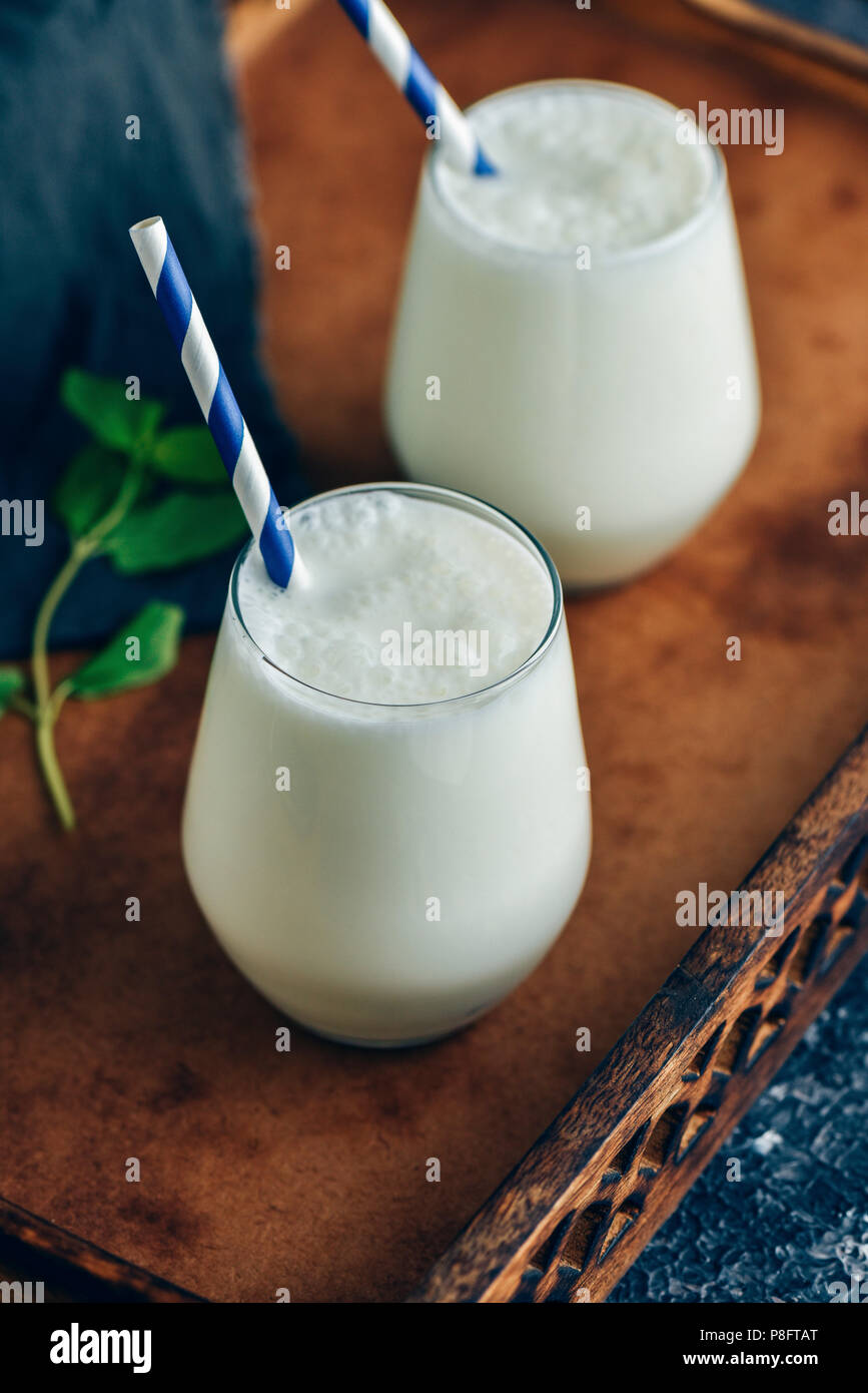 Bebida turco ayran en dos vasos con pajitas azul y blanco fotografiado en una bandeja de madera Foto de stock