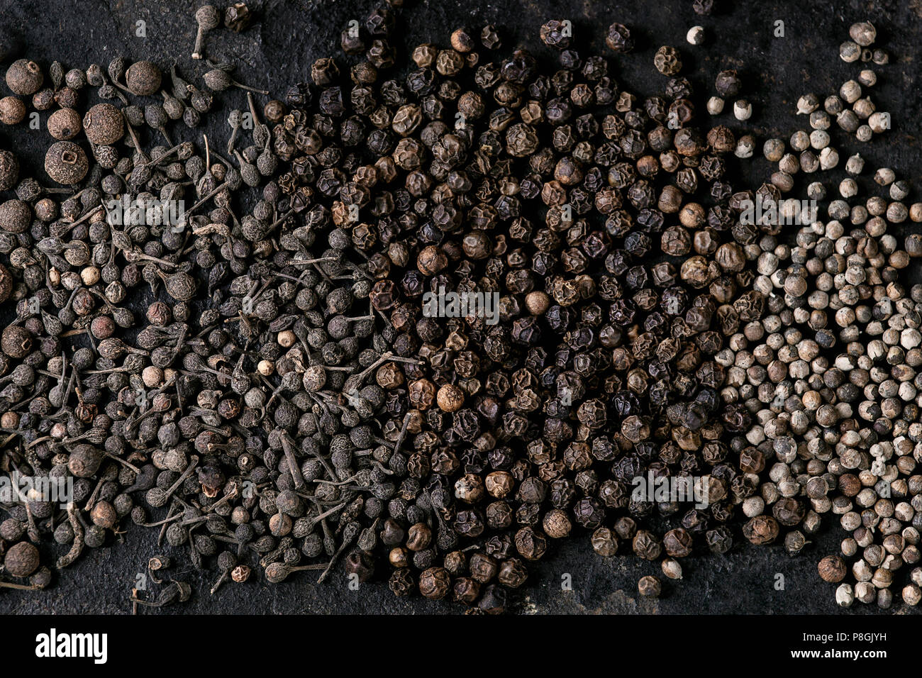 Variedad de pimiento negro pimienta de Jamaica, pimiento, monjes, los granos de pimienta pimienta negra de hierro antiguo sobre la textura de la superficie. Fondo de alimentos. Vista superior, el espacio. Foto de stock
