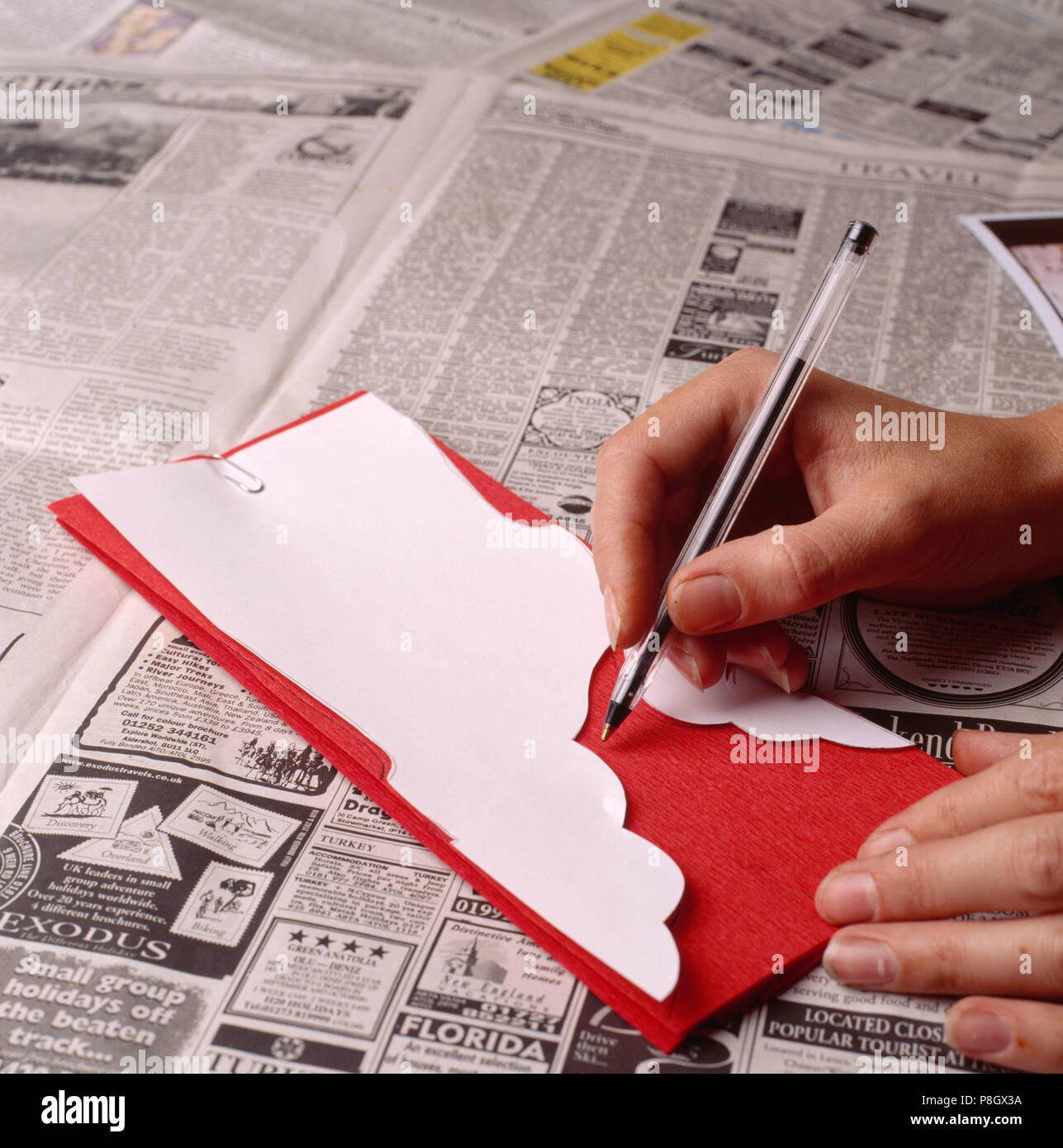 Close-up de manos utilizando un bolígrafo para dibujar alrededor tenplate blanco en papel crepé rojo SÓLO PARA USO EDITORIAL Foto de stock