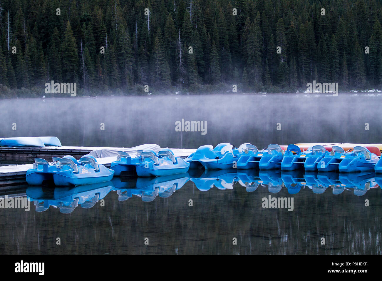 Botes de remos y reflexiones en las primeras horas de la mañana, en el lago Cameron, con niebla sobre el agua. Parque Nacional Waterton, Alberta, Canadá. Foto de stock