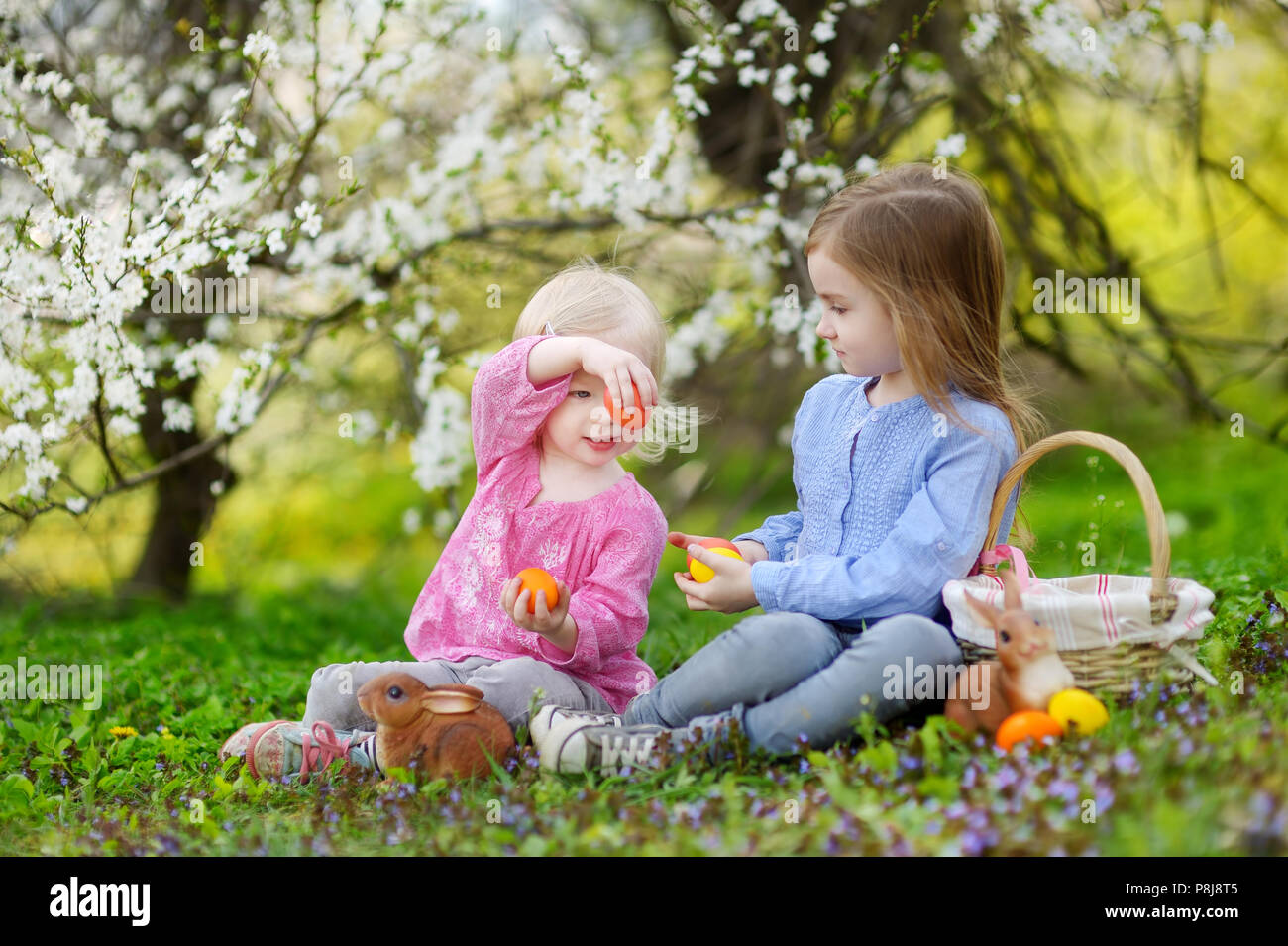 Adorable dos hermanitas jugando con los huevos de Pascua en la floración spring garden, el día de Pascua Foto de stock