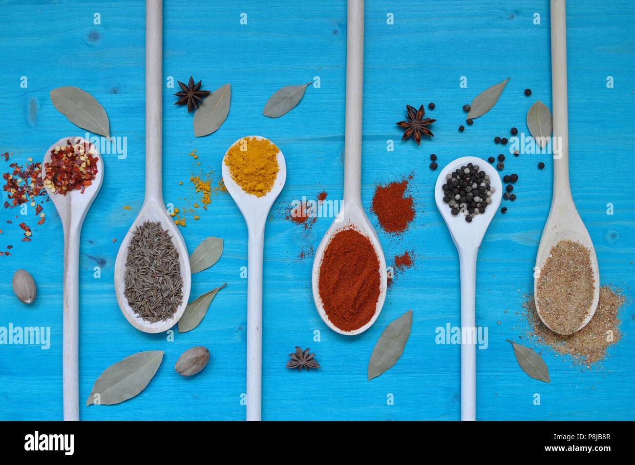 Concepto de tabla con coloridas especias en cucharas de madera sobre fondo azul, laicos plana Foto de stock