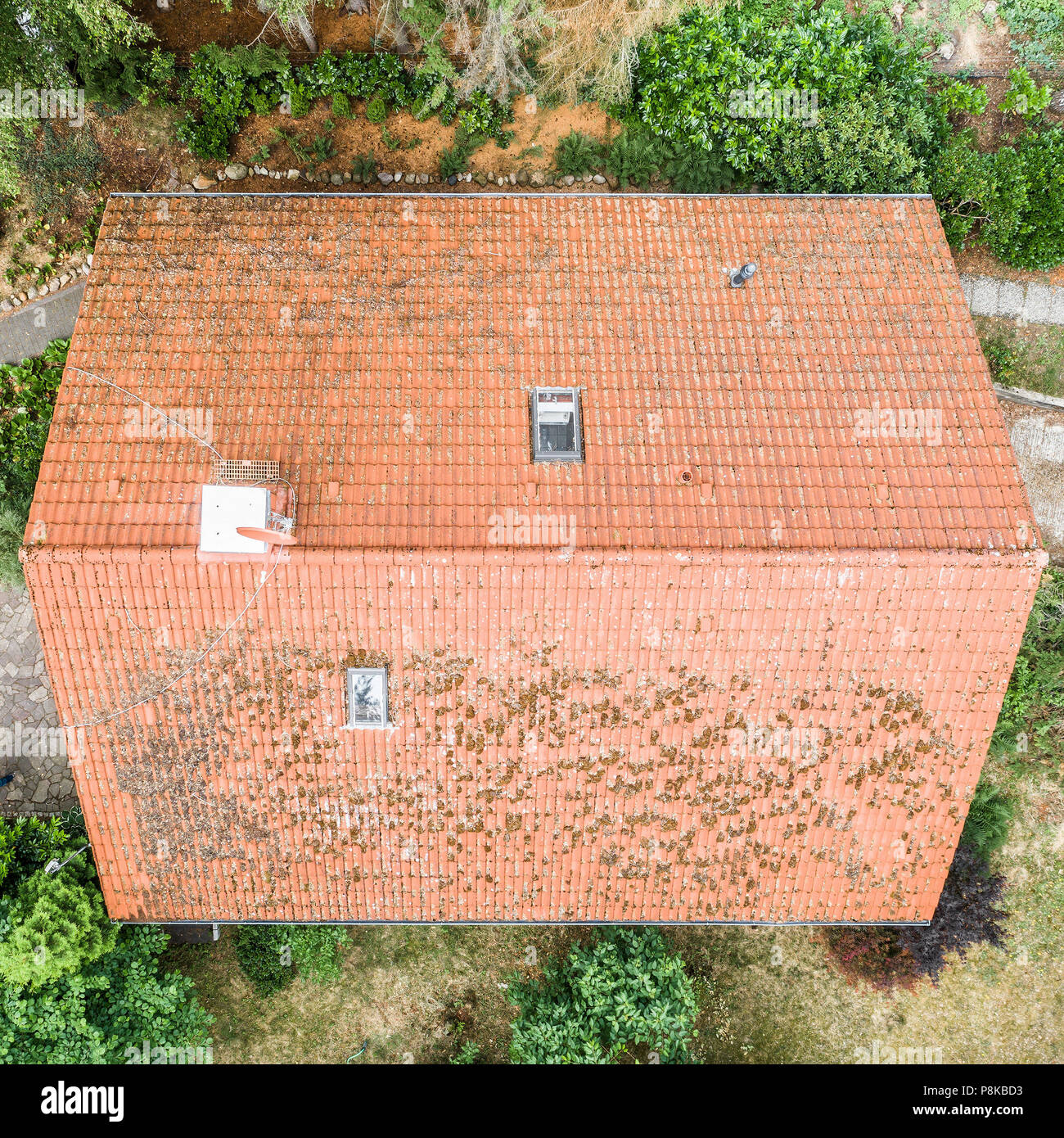 Vuelo sobre el techo rojo de una casa unifamiliar con una chimenea y una antena de satélite para la inspección, control y preparación para una reparación, wi Foto de stock