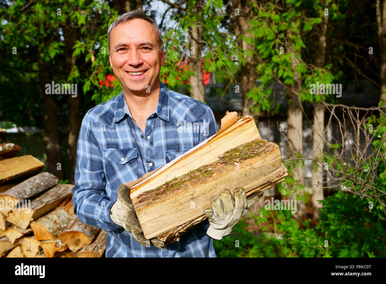 Un hombre de 50 años de edad caucásico vistiendo una camisa azul está sonriendo a nosotros mientras hinca su madera para la temporada de invierno, a fin de calentar la casa. Foto de stock