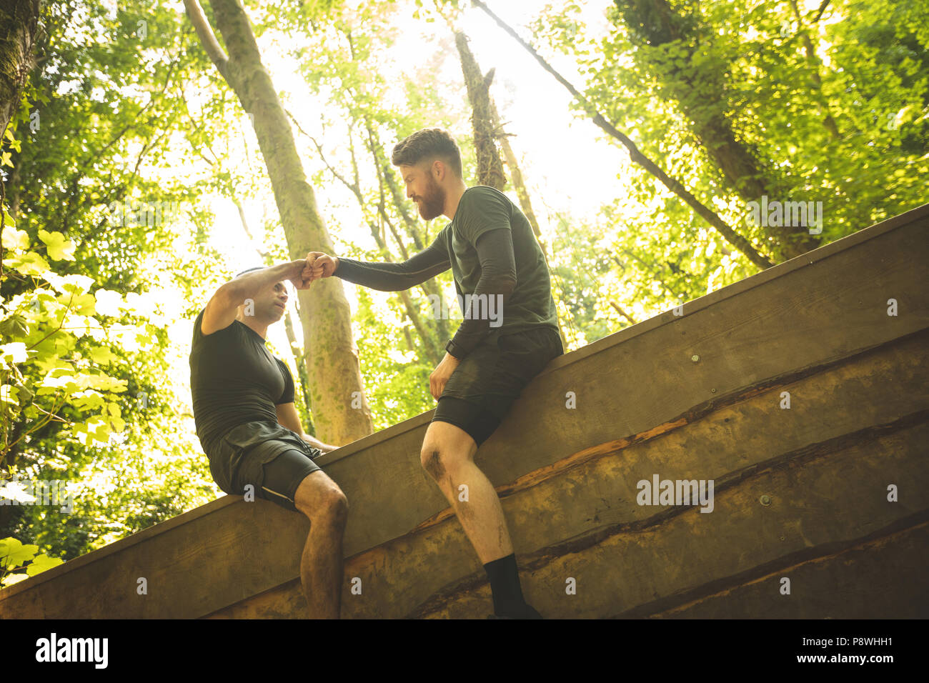 Colocar el hombre ayudando a su compañero de equipo para escalar una pared de madera Foto de stock