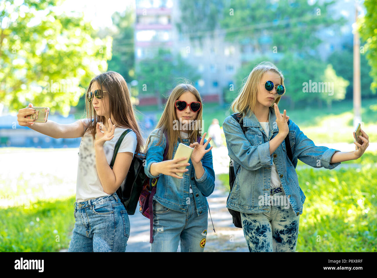 Tres chicas adolescentes. En denim ropa. Verano en la naturaleza. Tiene en  sus manos un smartphone. Se comunica con el Internet a través de una  videoconferencia. Video llamada en el teléfono. Fotografía