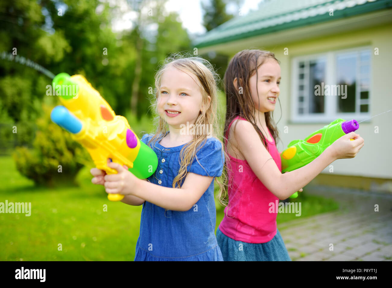 Adorable pequeño niñas jugando con pistolas de agua en los calurosos días  de verano. Lindo los niños se divierten con el agua de afuera. Divertidos  juegos de verano para niños Fotografía de