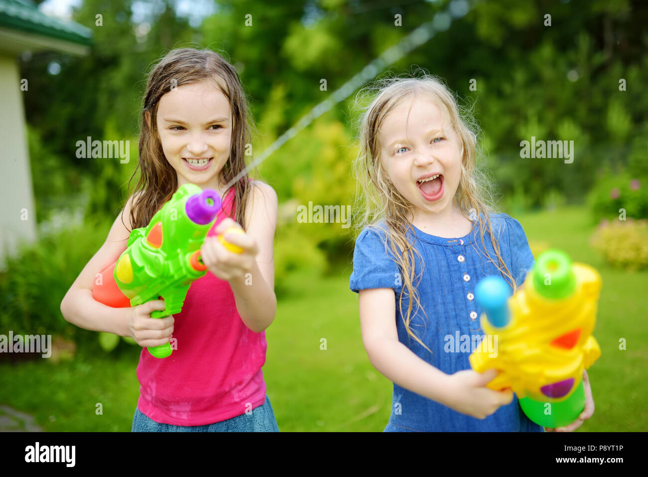 Adorable pequeño niñas jugando con pistolas de agua en los calurosos días  de verano. Lindo los niños se divierten con el agua de afuera. Divertidos  juegos de verano para niños Fotografía de