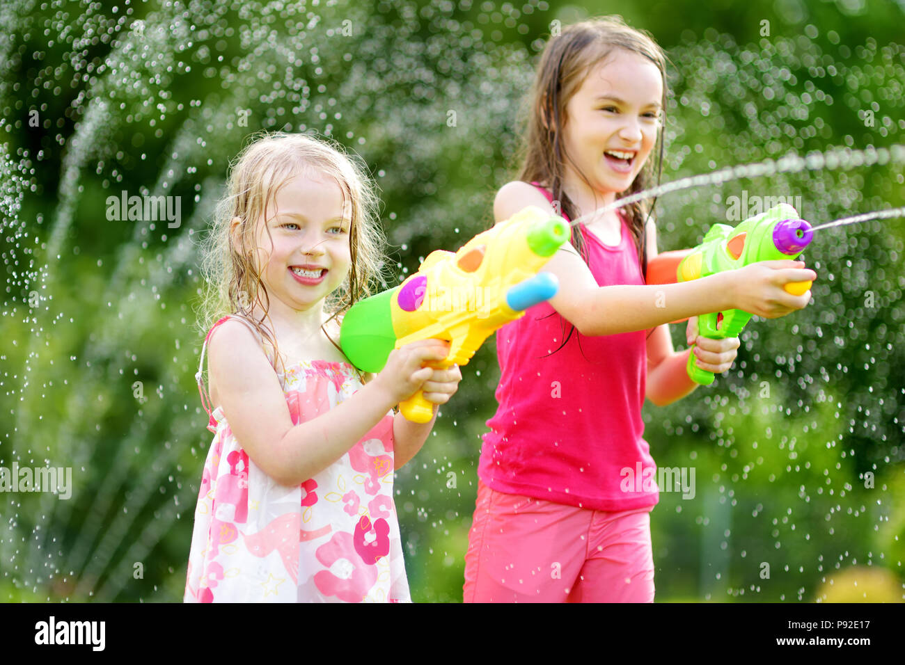 Adorable pequeño niñas jugando con pistolas de agua en los calurosos días de  verano. Lindo los niños se divierten con el agua de afuera. Divertidos juegos  de verano para niños Fotografía de