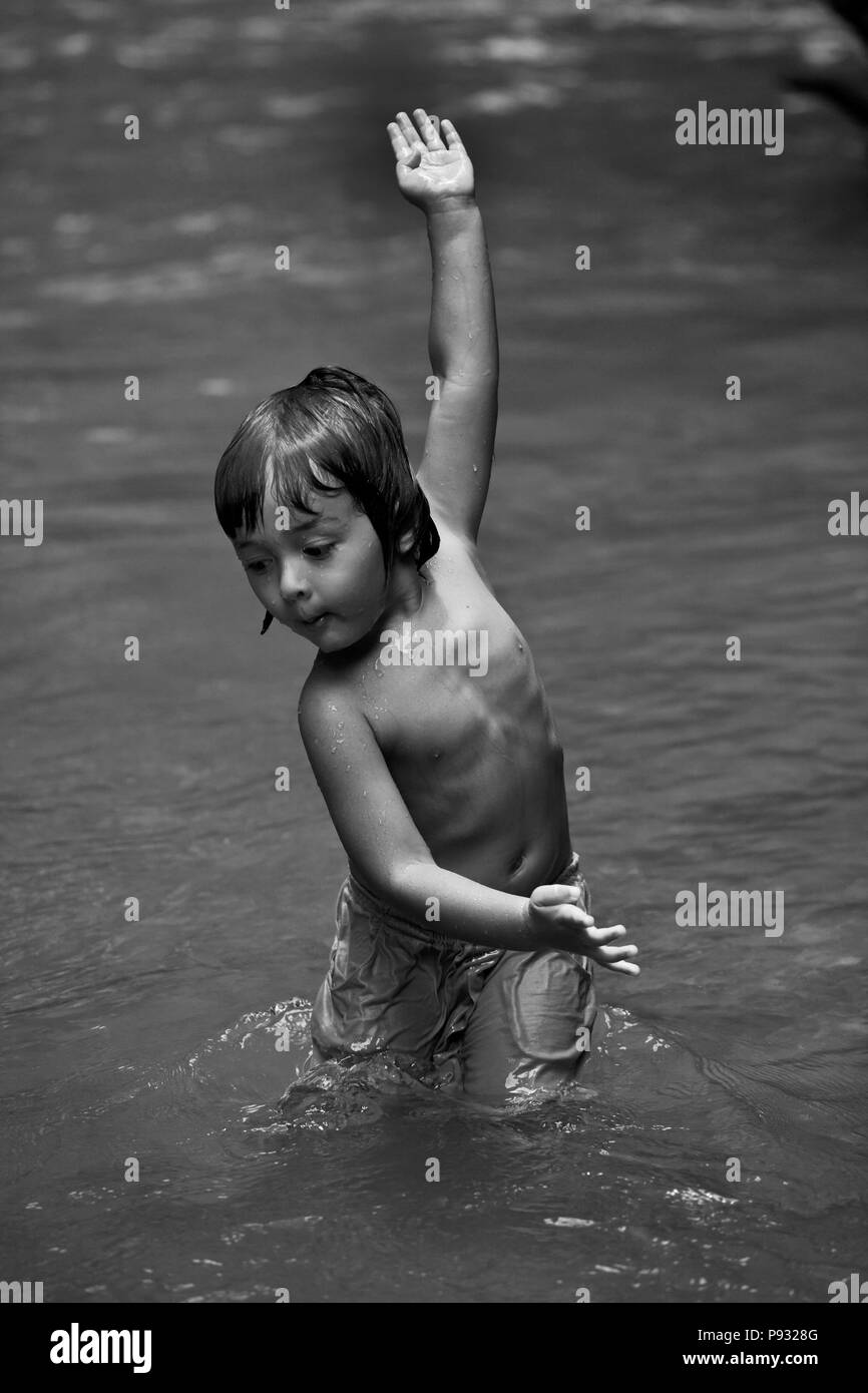 Un joven tailandés de media la mitad de los niños estadounidenses desempeña en un río tropical - Tailandia Foto de stock