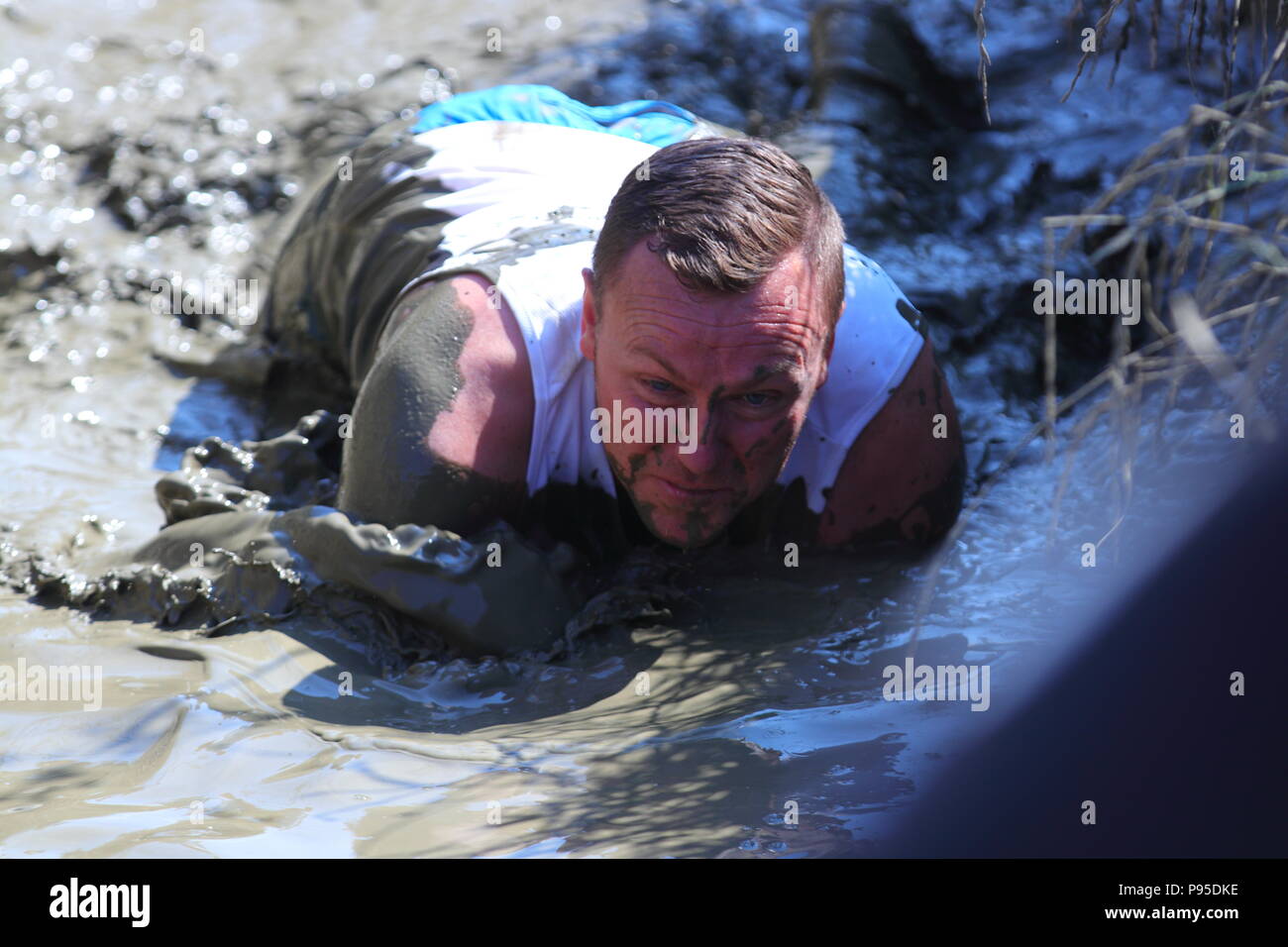 Un hombre se arrastra por el lodo durante un evento obstáculo fangosos en Leeds Foto de stock