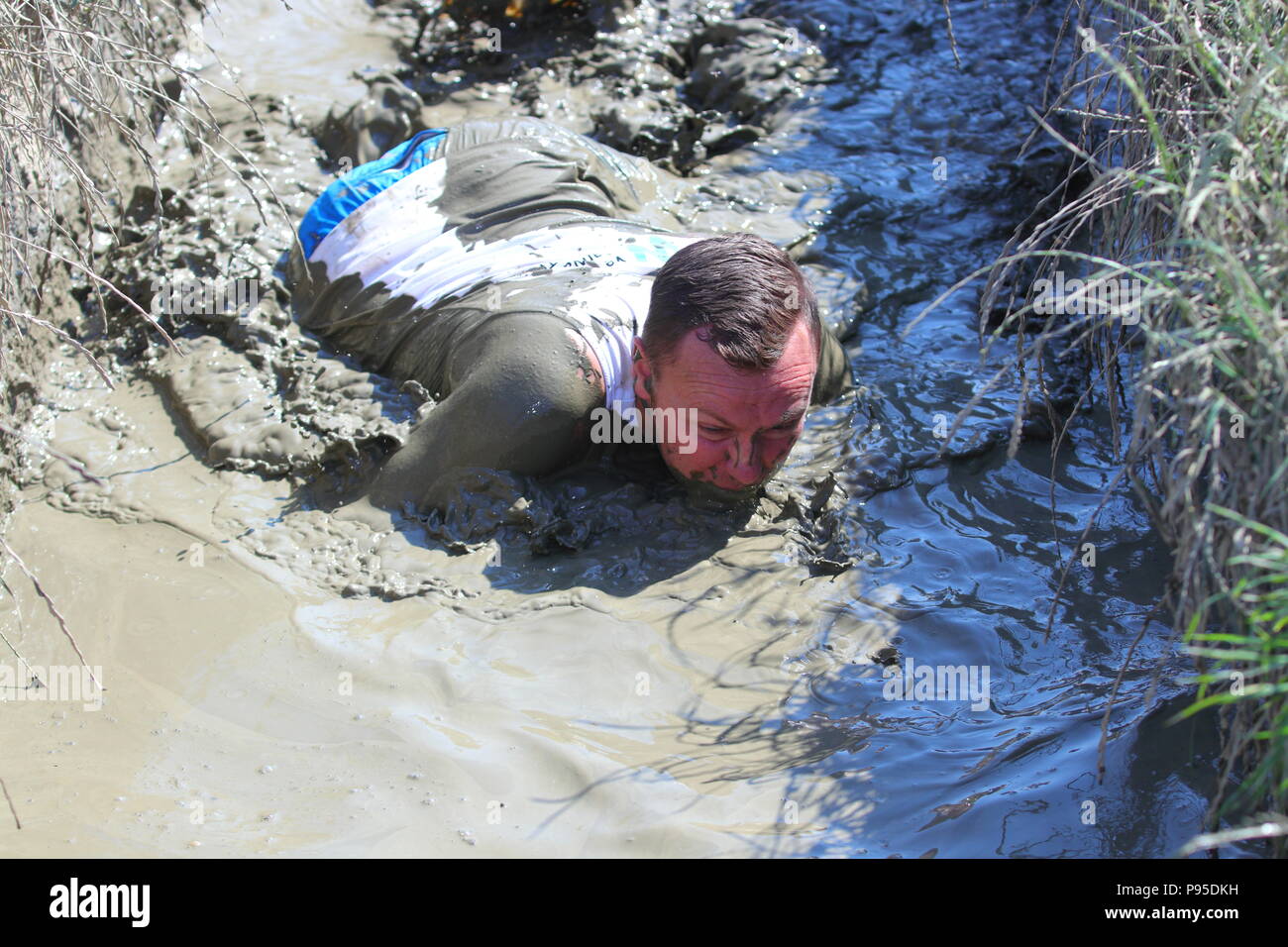 Un hombre se arrastra por el lodo durante un evento obstáculo fangosos en Leeds Foto de stock
